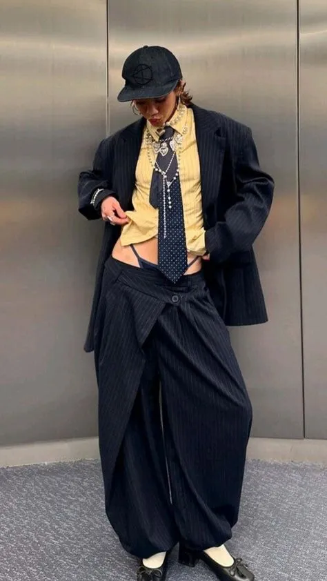 Corpcore aesthetic — The deconstructed pinstripe suit with a tie, blazer, and exposed underwear directly references the 'performing professional adulthood as a fashion statement' and 'flirts with the related Office Siren trend' aspects of Corpcore.