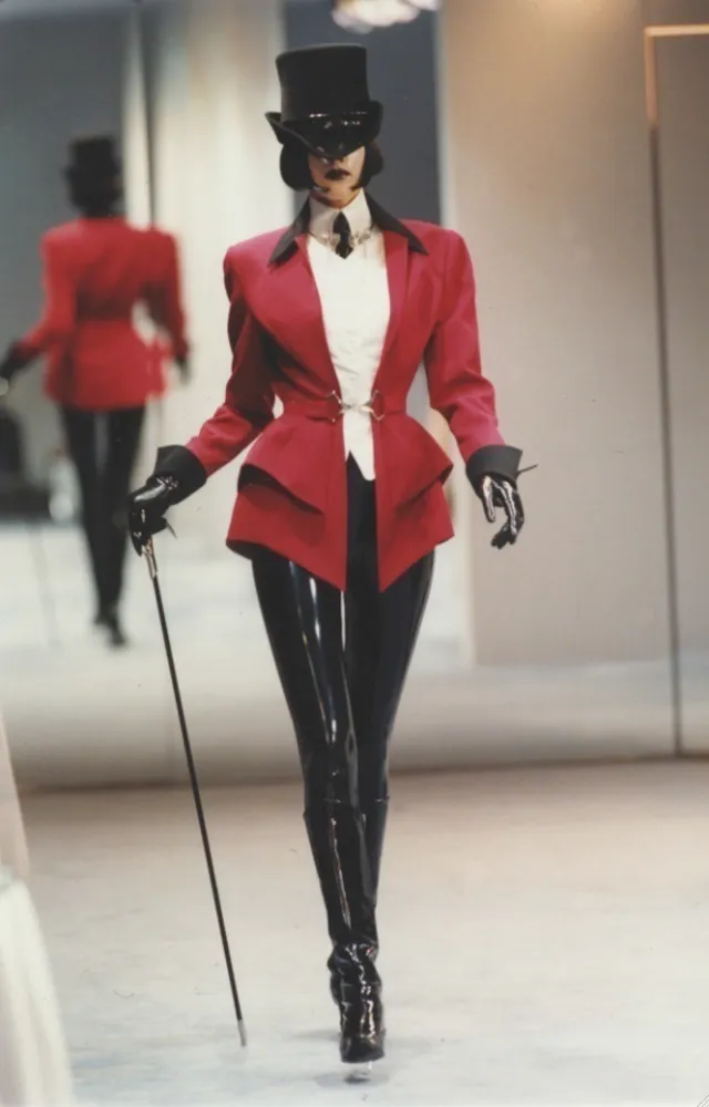 Dark Cabaret aesthetic — The ringmaster-style tailcoat, top hat, pinstripe trousers, and cane are direct matches to the signature garments and theatricality described.