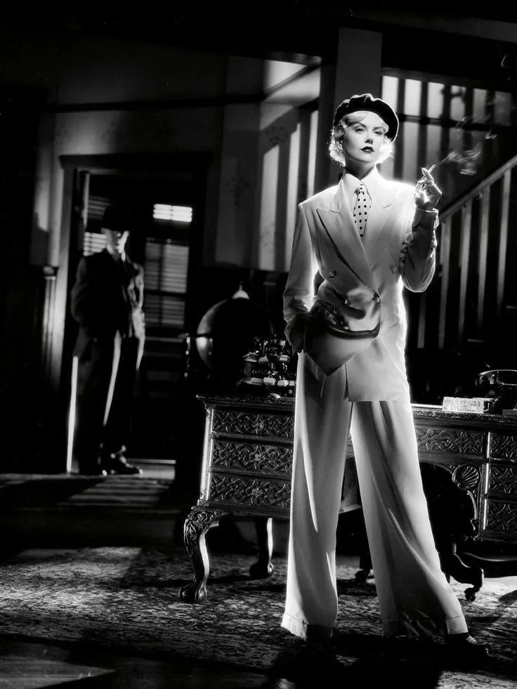 Film Noir aesthetic — Woman in a sharp, tailored suit with a tie and beret, embodying the masculine-coded fashion of the era and genre.