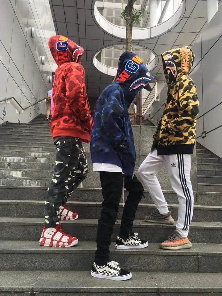 Hypebeast aesthetic — Multiple BAPE shark hoodies in iconic camo patterns, paired with sneakers and graphic elements, directly embody the visual signature and canonical brands of Hypebeast.