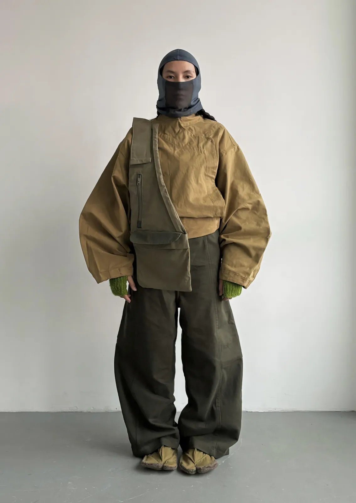 Industrial aesthetic — The utilitarian jacket, cargo pants, balaclava, and crossbody bag strongly evoke the factory-issue and military webbing aspects of the industrial aesthetic.