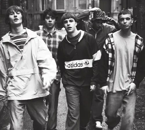 Lad Culture aesthetic — The group's attire, including the Adidas jacket, plaid shirt, and jeans, along with the haircuts, is a strong visual representation of the Britpop era and Lad Culture.