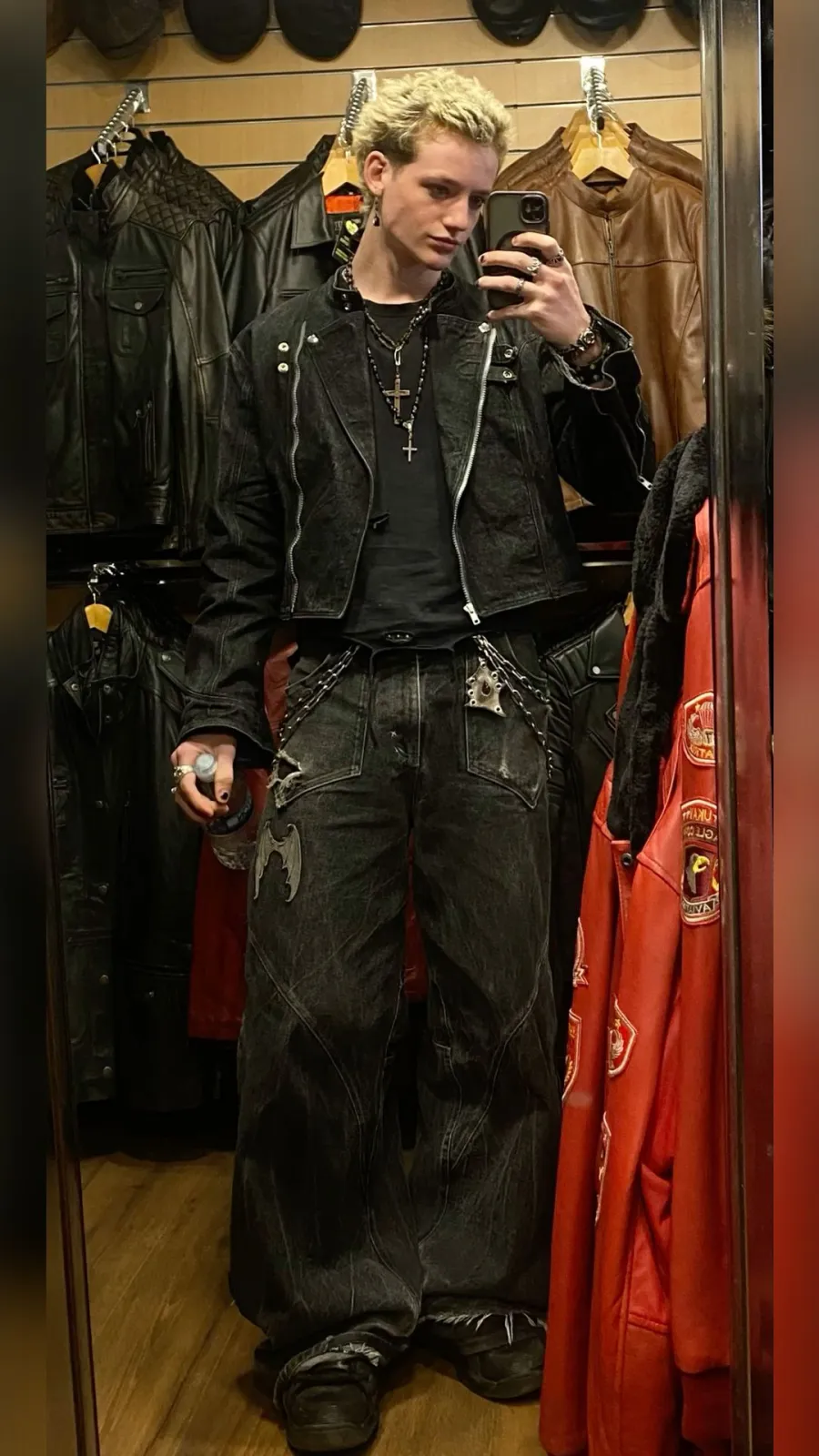Metalhead aesthetic — The outfit features a black leather jacket, distressed black jeans with chain detailing, and heavy silver jewelry, all core elements of the metalhead aesthetic as described.