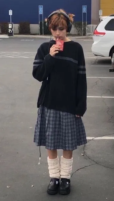 Midwest Emo aesthetic — The plaid pleated skirt, layered long-sleeve shirt, leg warmers, and headphones strongly evoke the 2010s revival of the Midwest Emo visual signature.