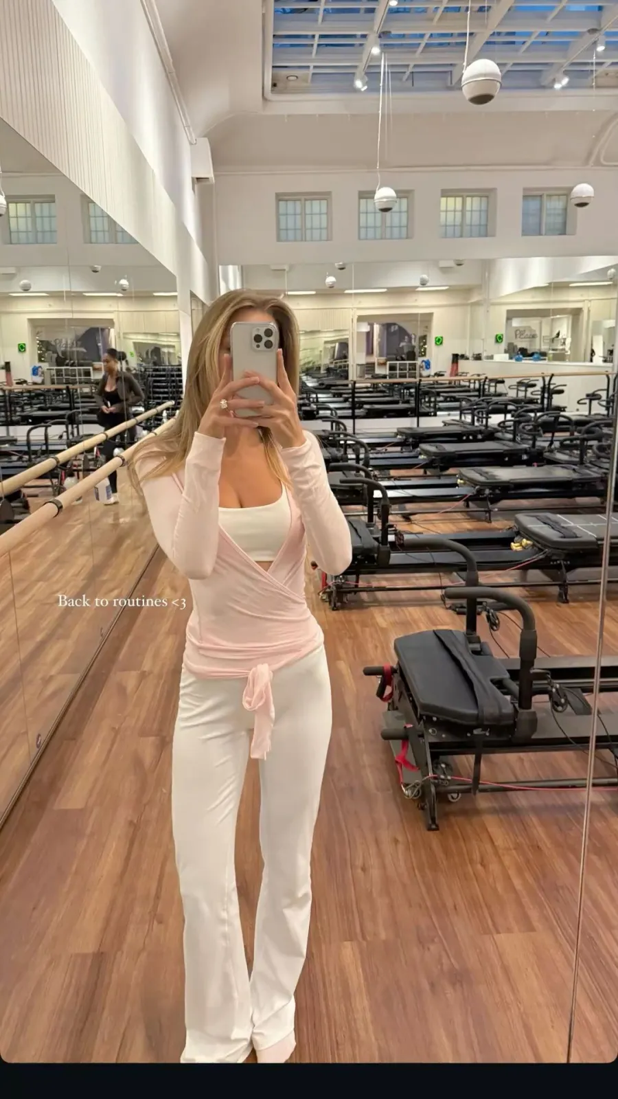 Pilates Princess aesthetic — The pastel pink wrap top and white flared pants, combined with the Reformer Pilates studio background, perfectly capture the essence and specific context of the Pilates Princess aesthetic.