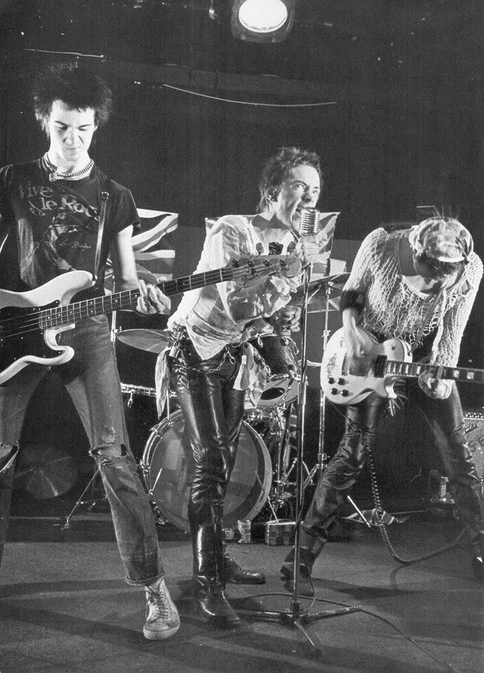 Punk aesthetic — Captures the raw energy of punk with torn band tees, leather trousers, ripped jeans, and a live performance setting, directly referencing the movement's origins.