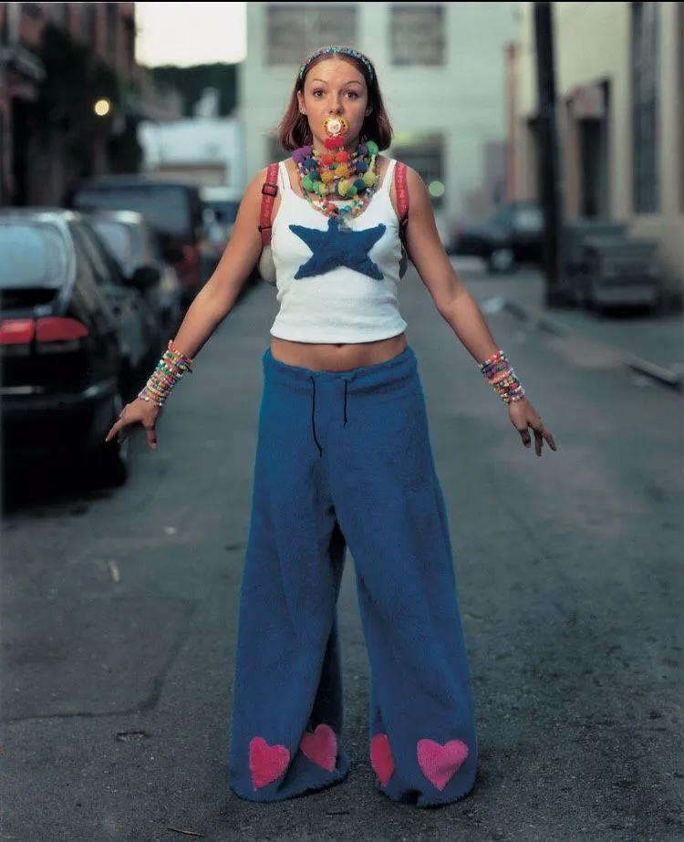 Rave aesthetic — The fuzzy blue pants with heart appliques, kandi bracelets, and pacifier are direct references to 90s rave culture and PLUR.