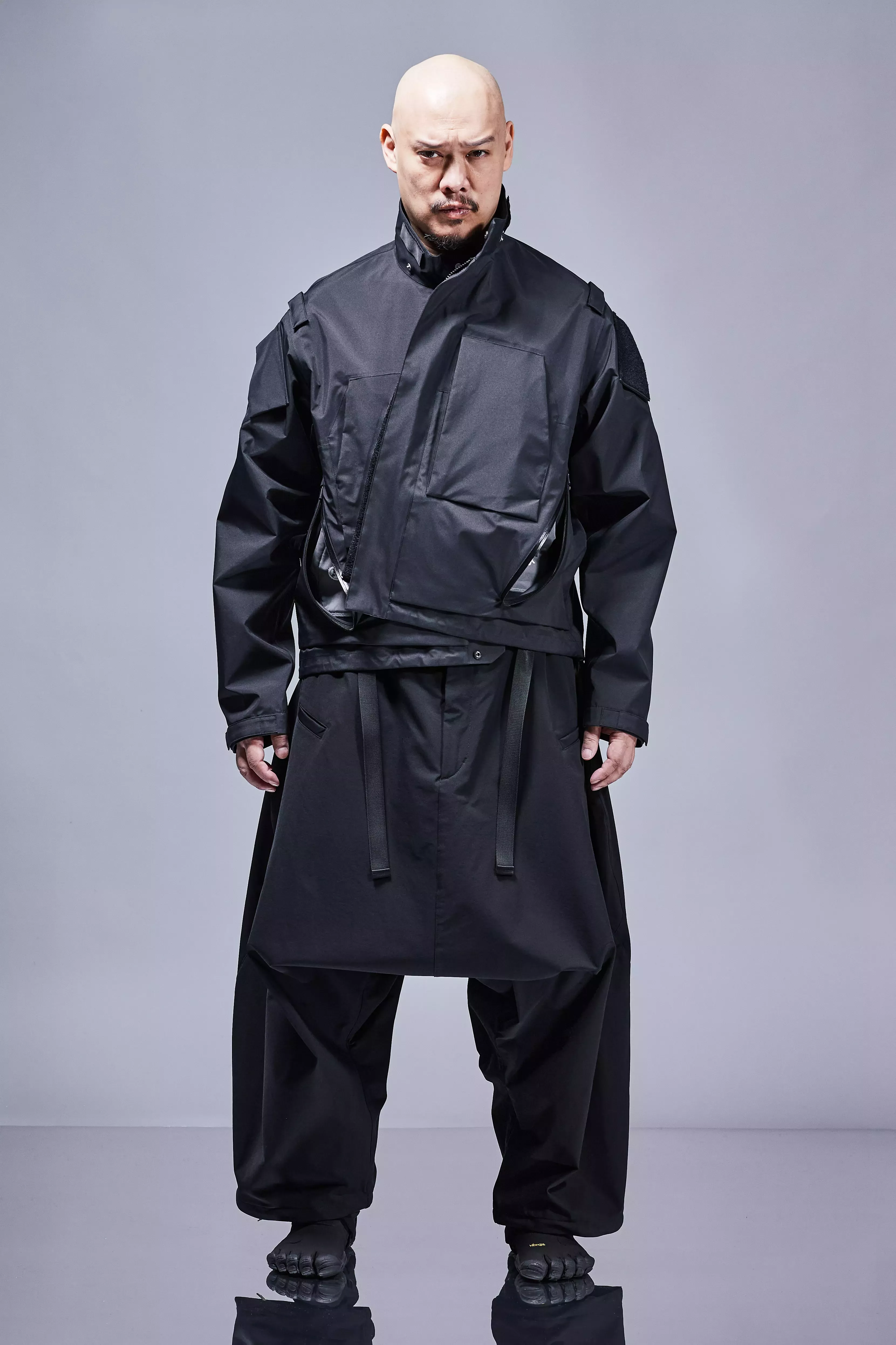 Techwear aesthetic — The image features a monochrome palette, technical fabrics, modular construction with external pockets and straps, and a sci-fi militaristic silhouette, directly aligning with the description's core elements.