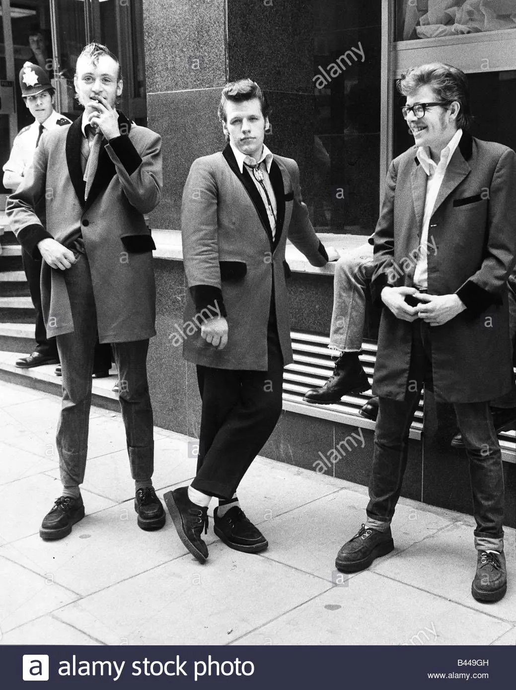 Teddy Boys aesthetic — All three individuals are wearing classic Teddy Boy attire: Edwardian drape jackets with velvet collars and cuffs, drainpipe trousers, and brothel creepers.