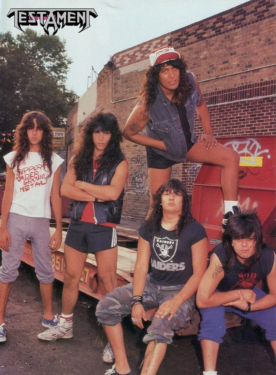 Thrash Metal aesthetic — This image directly features the band Testament, a canonical reference, and the individuals are dressed in signature Thrash Metal attire like band tees, denim vests, and ripped jeans.