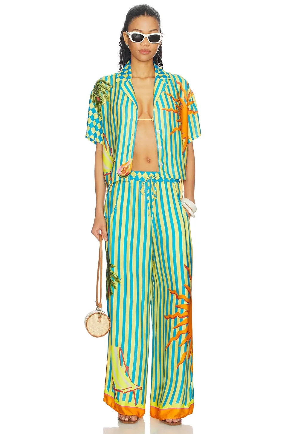 Tropical aesthetic — This image perfectly captures the aesthetic with a palm and sun print shirt-and-pants set in the signature turquoise and sunset orange palette, embodying the 'Hawaiian-shirt-and-sundress dressing' and 'equatorial island-coded fashion'.